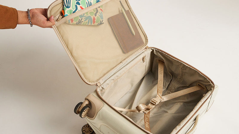 Open CALPAK Terra 35L Soft Sided in beige White Sands suitcase with a floral-patterned pouch inside on a light background