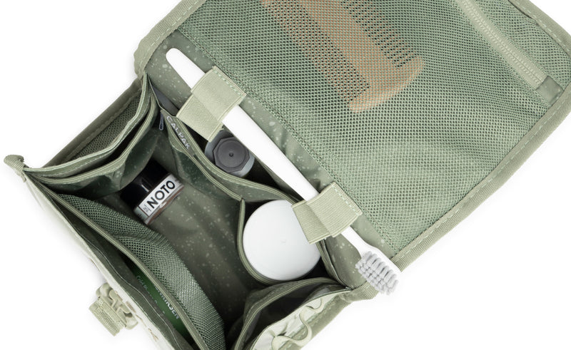 CALPAK Hanging Toiletry Bag in green Juniper opened view with toiletries inside, such as a white toothbrush and a brown comb