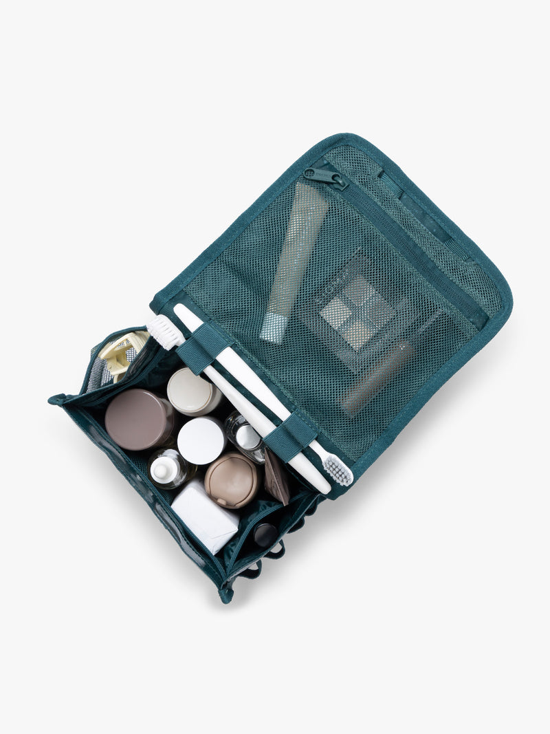 CALPAK Terra Hanging Toiletry Bag storing makeup and toiletries in blue green Kale on a white background