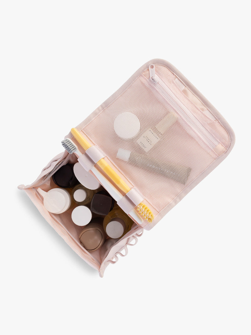 Toiletry items in the CALPAK Terra Hanging Toiletry Bag in light pink Shell Pink with front buckle