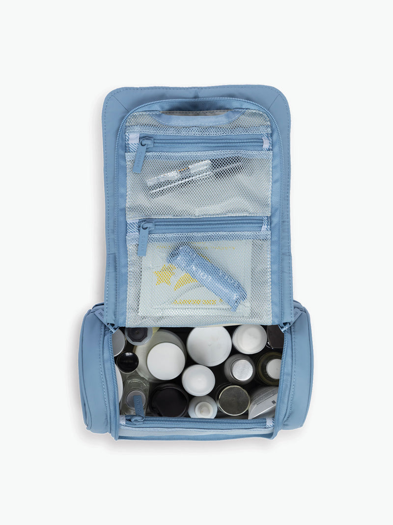 Opened with toiletries of the CALPAK Luka Hanging Toiletry Bag in light blue French Blue