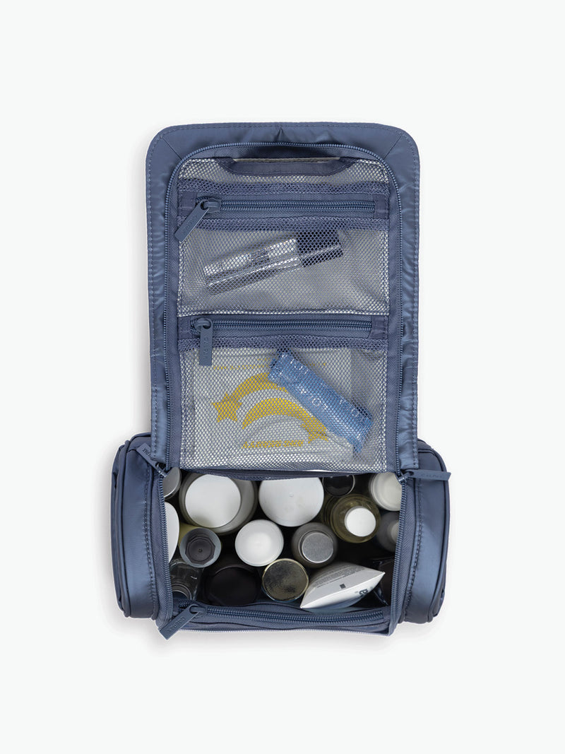 Toiletries inside the CALPAK Luka Hanging Toiletry Bag in metallic dark blue material in Metallic Indigo