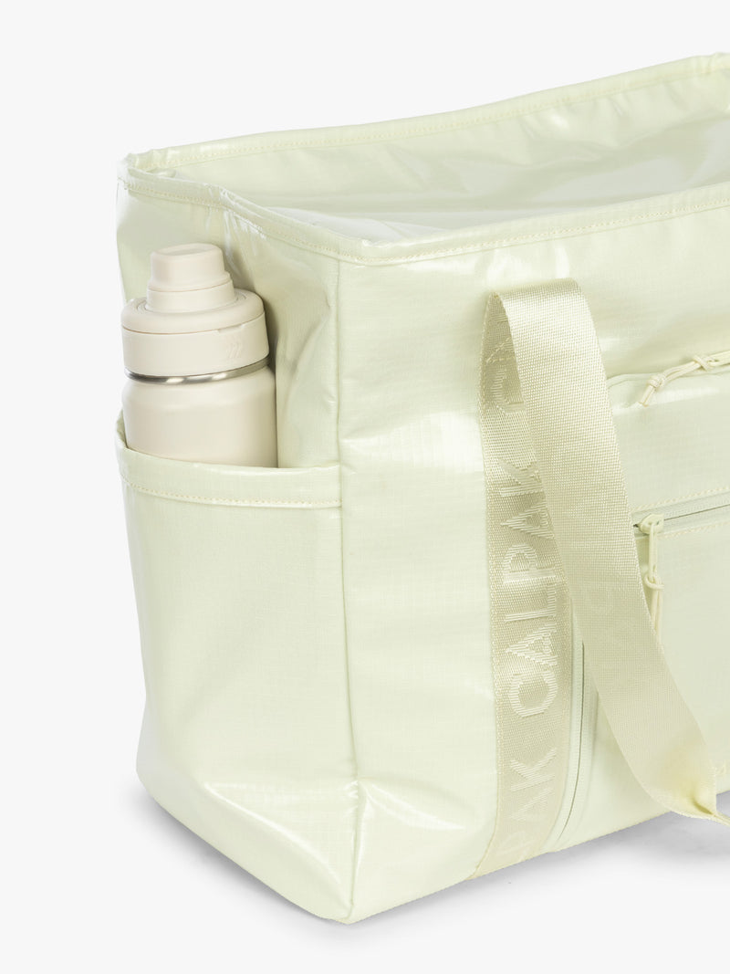 Side water bottle pocket of the CALPAK Terra 35L Tote Bag with multiple pockets and shoulder straps in shiny light green Celadon on a white background