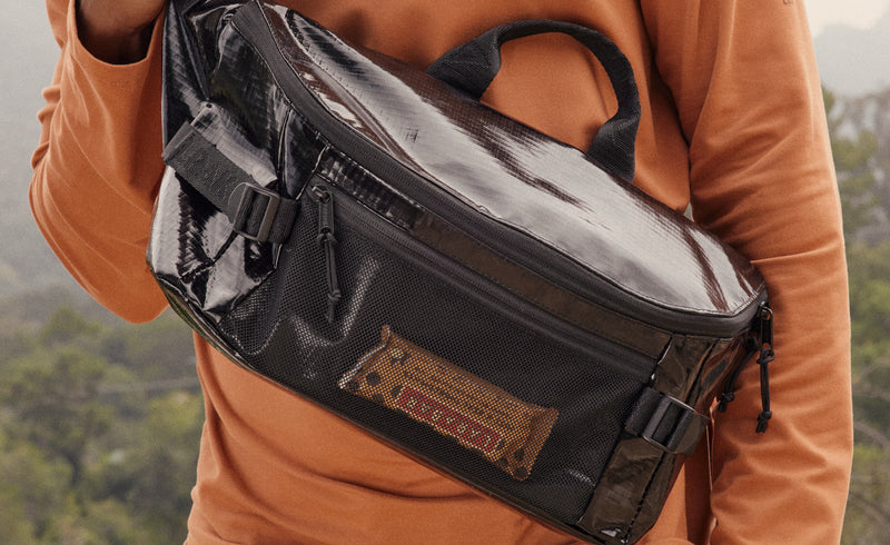 Lifestyle image of Terra Sling Bag in Cacao on model with orange long sleeve shirt