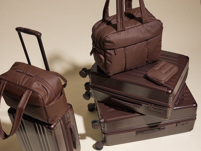Stack of brown CALPAK suitcases, organizers and bags on a beige background