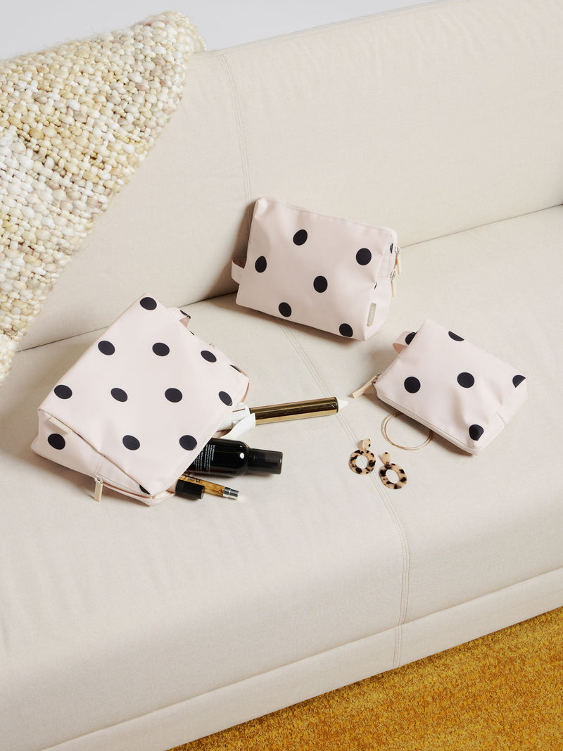 A polka-dot dopp kit set arranged on a neutral sofa, paired with beauty essentials like lip gloss and perfume—blending style and function for the best dopp kit experience.