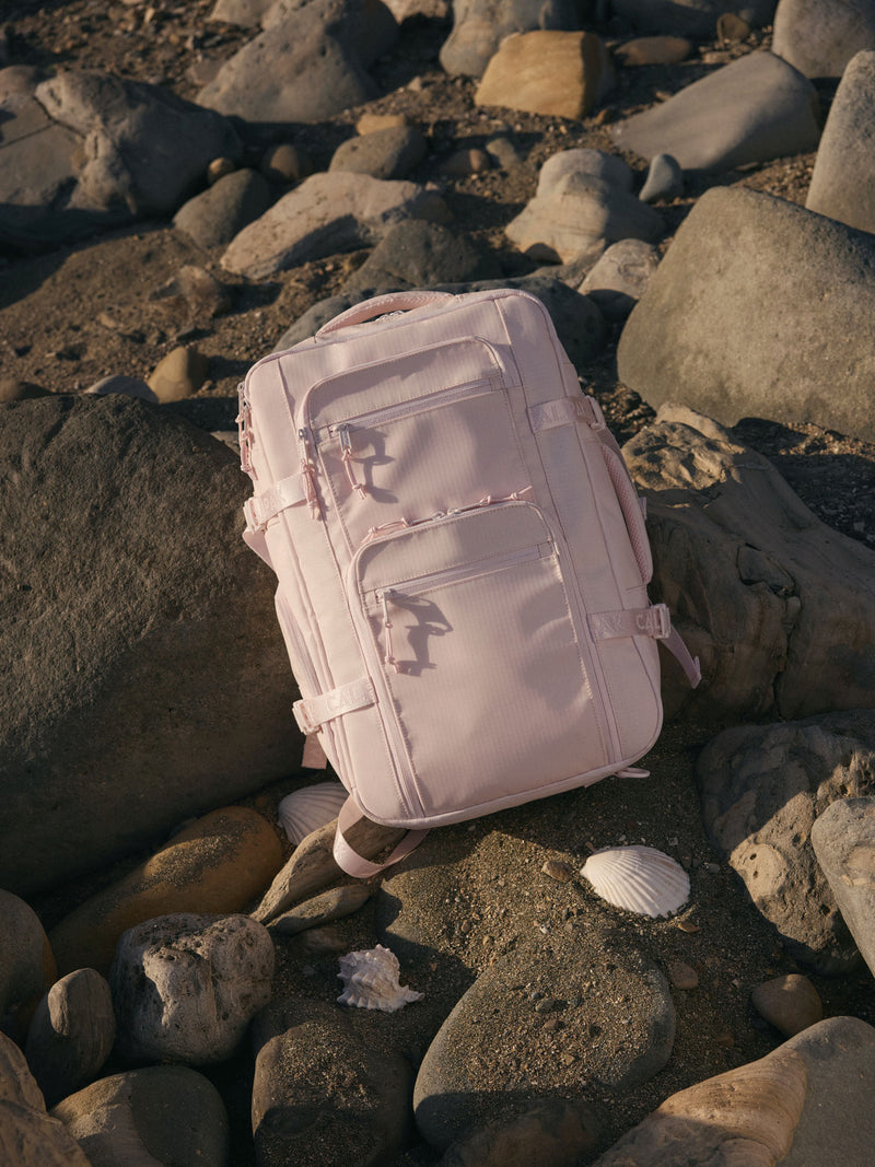 Pink Seashell CALPAK Terra 26L Backpack on a rocky beach