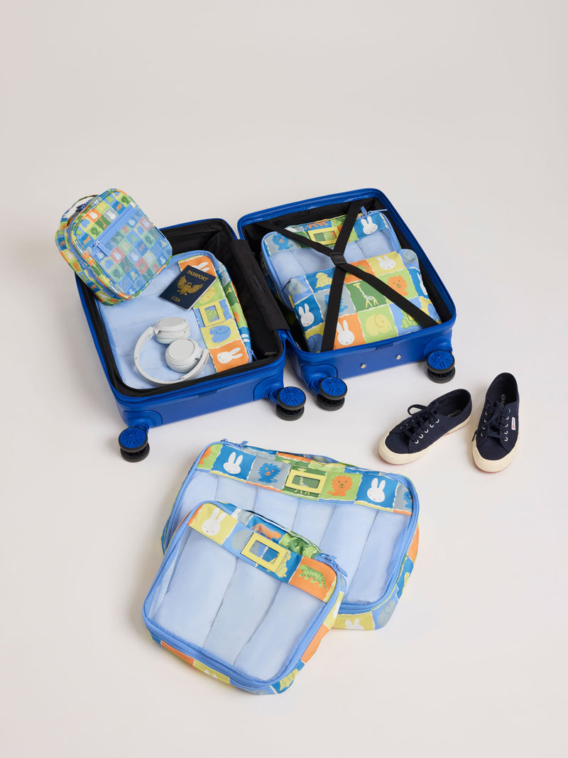 Colorful travel set of CALPAK Packing Cubes in colorful blue pouches with Miffy and animal pattern on a white background including a suitcase, shoes, and a bag on a light gray background