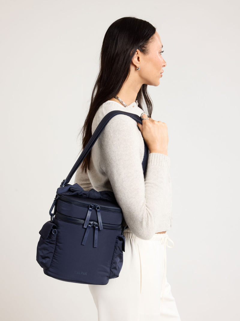 Woman wearing the CALPAK Insulated Baby Bottle Bag in blue navy