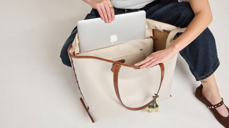 Person placing a laptop into a beige CALPAK Colette Laptop Tote bag on a light background