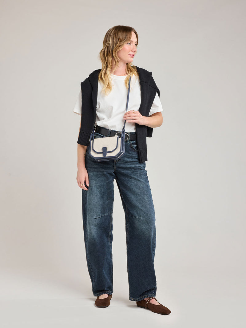 Woman wearing CALPAK Colette Canvas Crossbody Wallet Bag in Natural Brown with beige canvas material and blue finishing