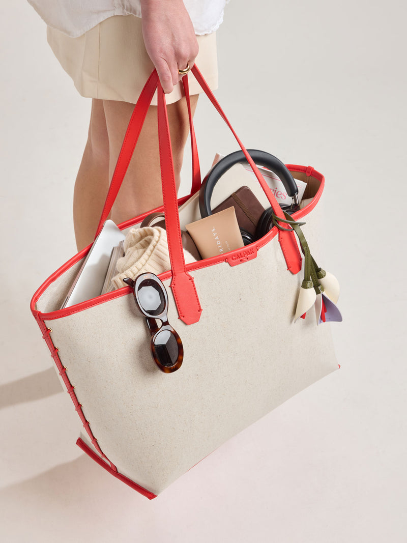 Model holding CALPAK Colette 15" Canvas Laptop Tote in beige canvas material  with red finishing in Natural Tomato