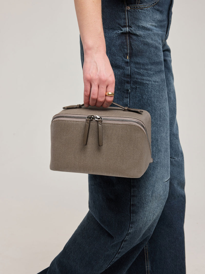 Woman wearing CALPAK Colette Lay-Flat Canvas Toiletry Bag in brown Mushroom canvas material