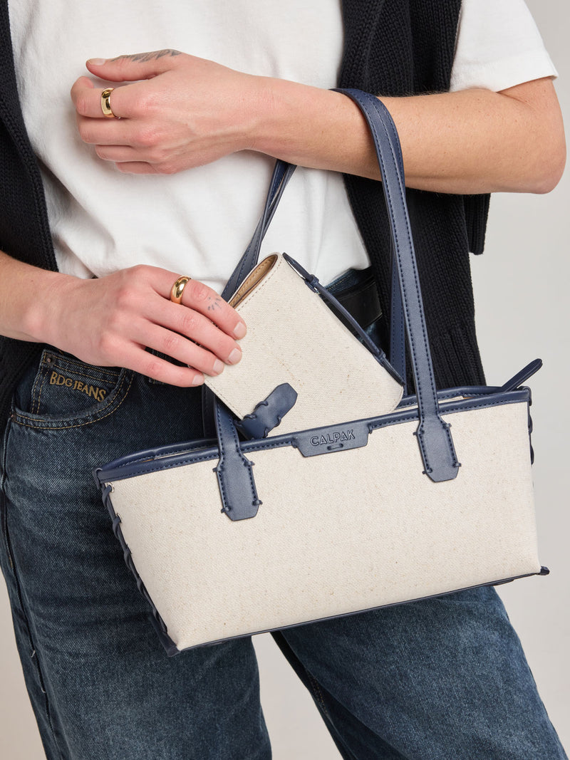 Model putting in bag the CALPAK Colette Multi Passport Wallet in beige canvas material and blue finishings in Natural Navy
