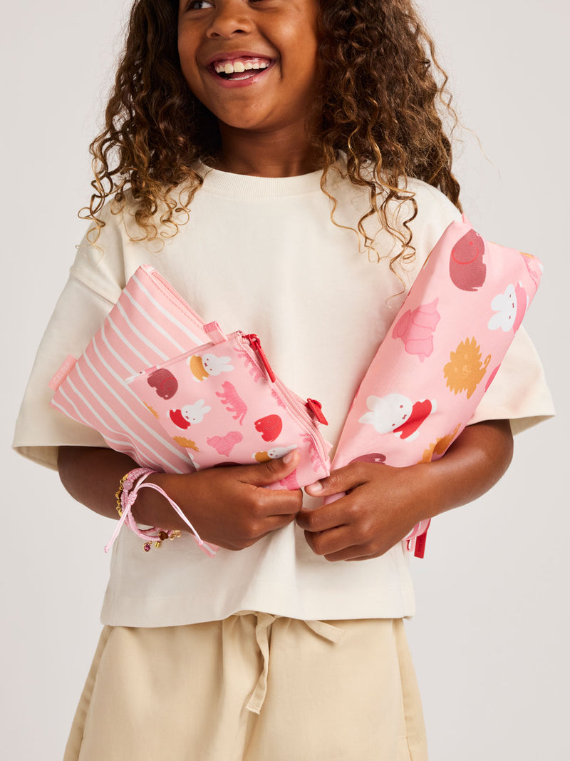 Child holding pink set of pink and white colorful children's pouches with Miffy and animal patterns for the CALPAK Compakt Zip Pouch Set on a white background