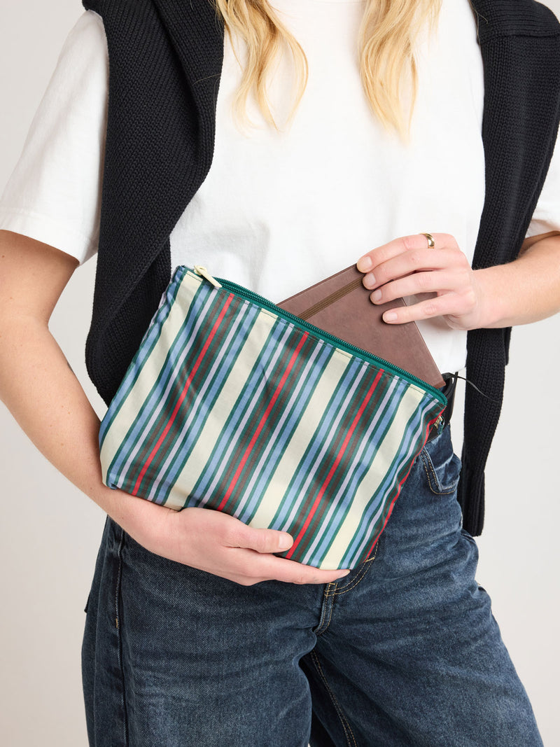 Person adding item in CALPAK Compakt ZIppered Pouch Set in multicolor stripes