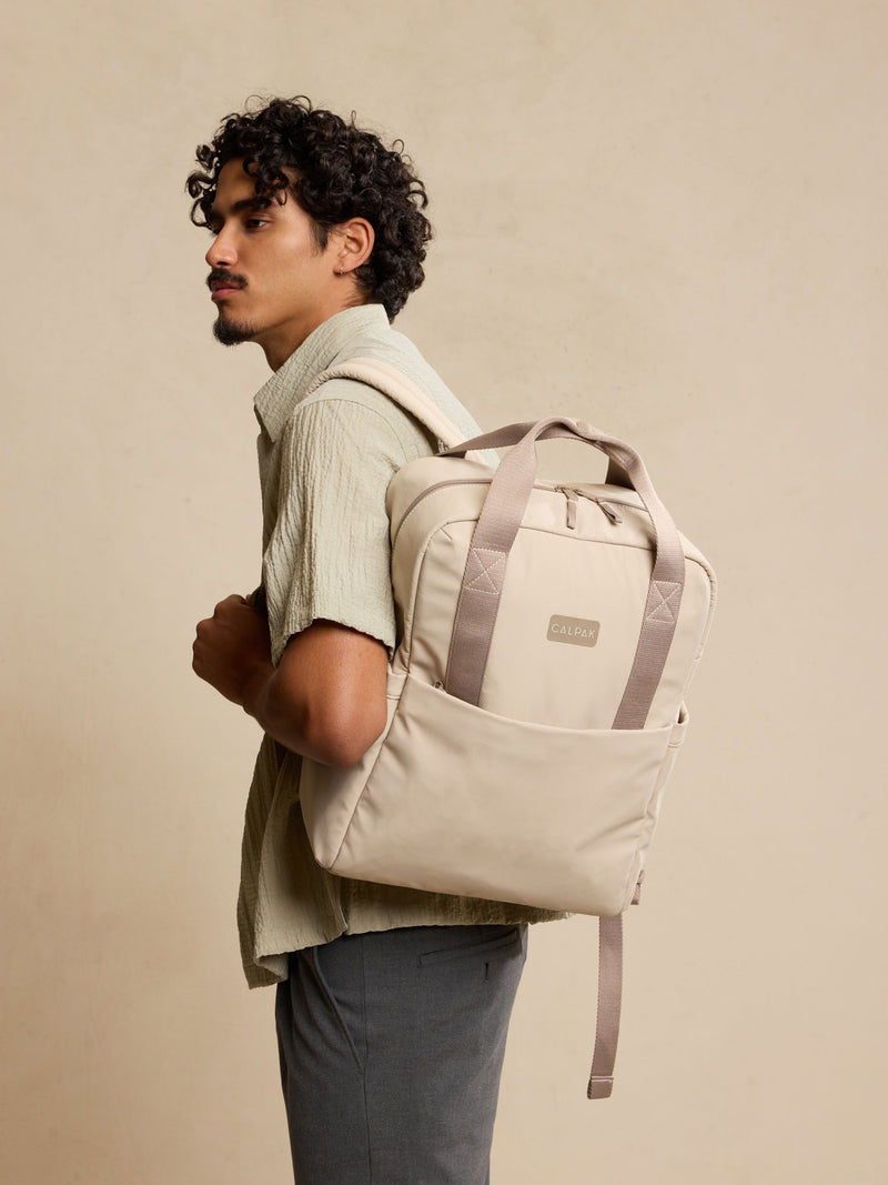 CALPAK Connect Laptop Backpack in grey beige Greige being worn by model  on a beige background