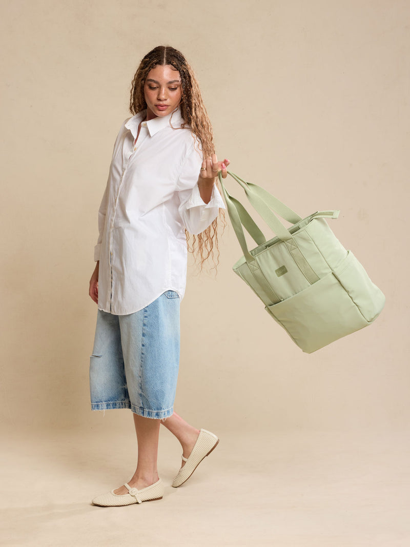 CALPAK Zippered Laptop Tote Bag in light green Meadow on a beige background being held by a model