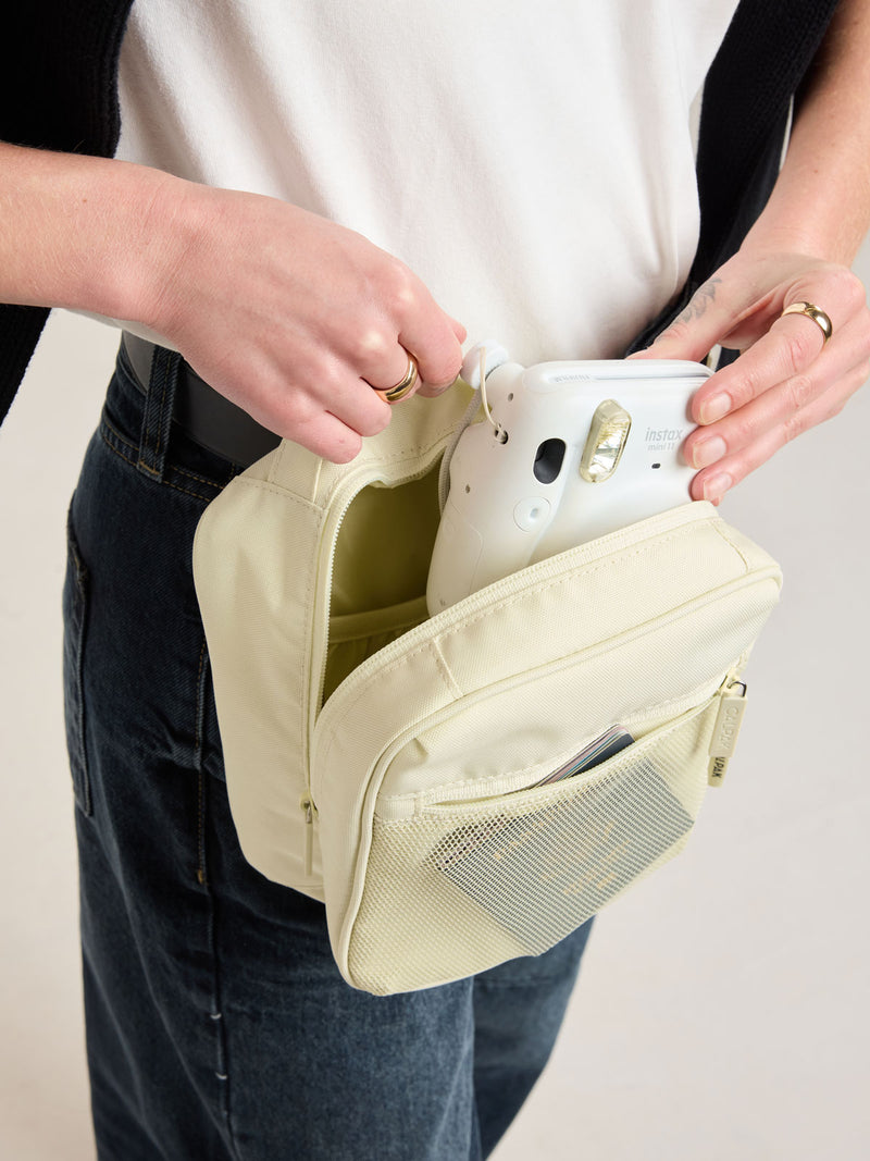 Person putting a polaroid camera into CALPAK Everything Cube in light green Celadon