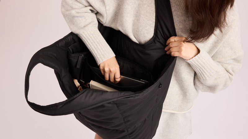 Person putting a laptop in the CALPAK Luka Everything Tote Bag in Black with a plain background