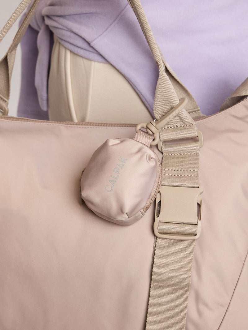Model holding CALPAK Fit Zip Bag Charm in grey beige Greige with hook and zipper