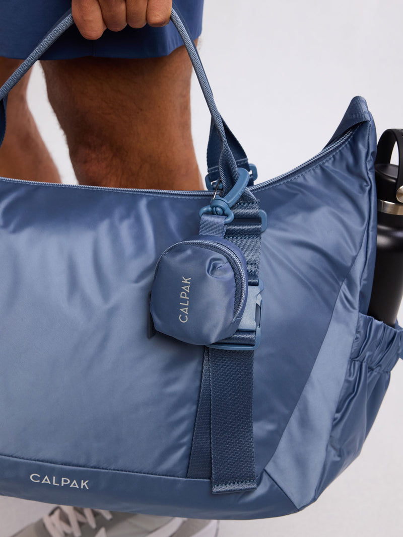 Model holding CALPAK Fit Zip Bag Charm in dark blue Indigo with hook and zipper
