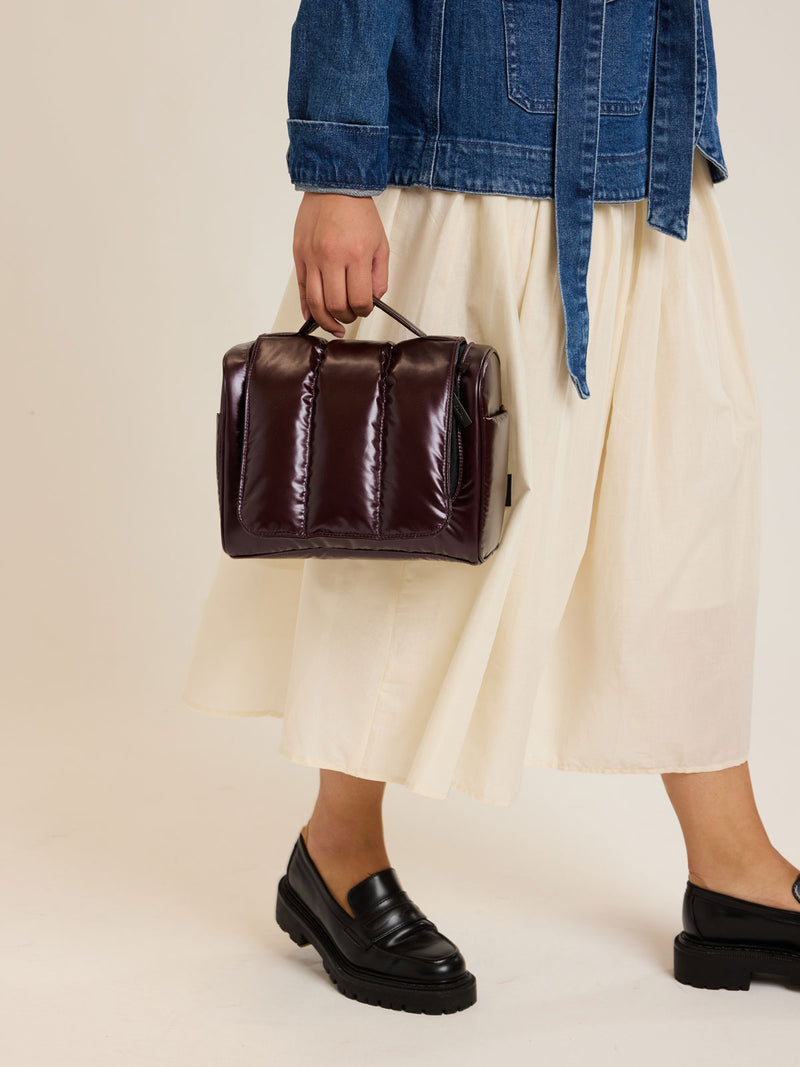 Model carrying the CALPAK Luka Hanging Toiletry Bag in maroon Glazed Dark Cherry