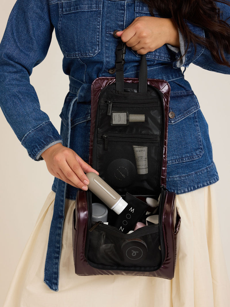 Model packing the CALPAK Luka Hanging Toiletry Bag in maroon Glazed Dark Cherry