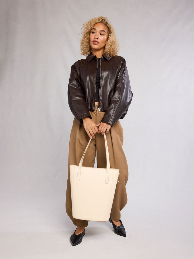 Woman holding the CALPAK Haven 14" Haven Laptop Tote in white beige Buttercream