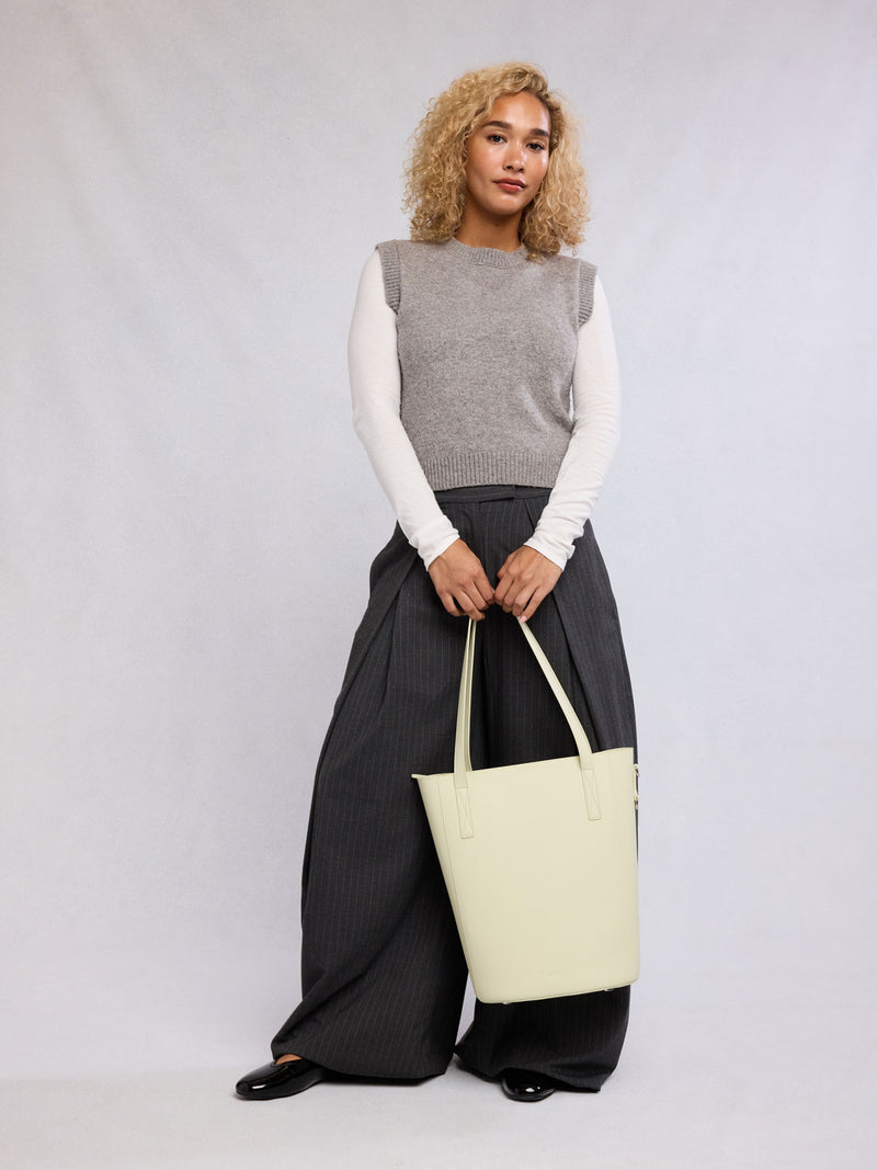 Woman holding the CALPAK Haven 14" Haven Laptop Tote in light green Celadon
