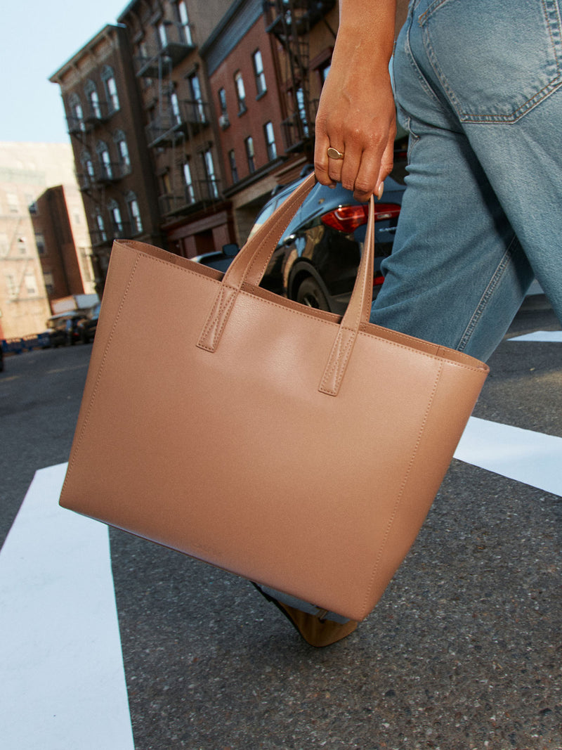 Model holding the straps of the CALPAK Haven 15 inch Laptop Tote in beige Taupe