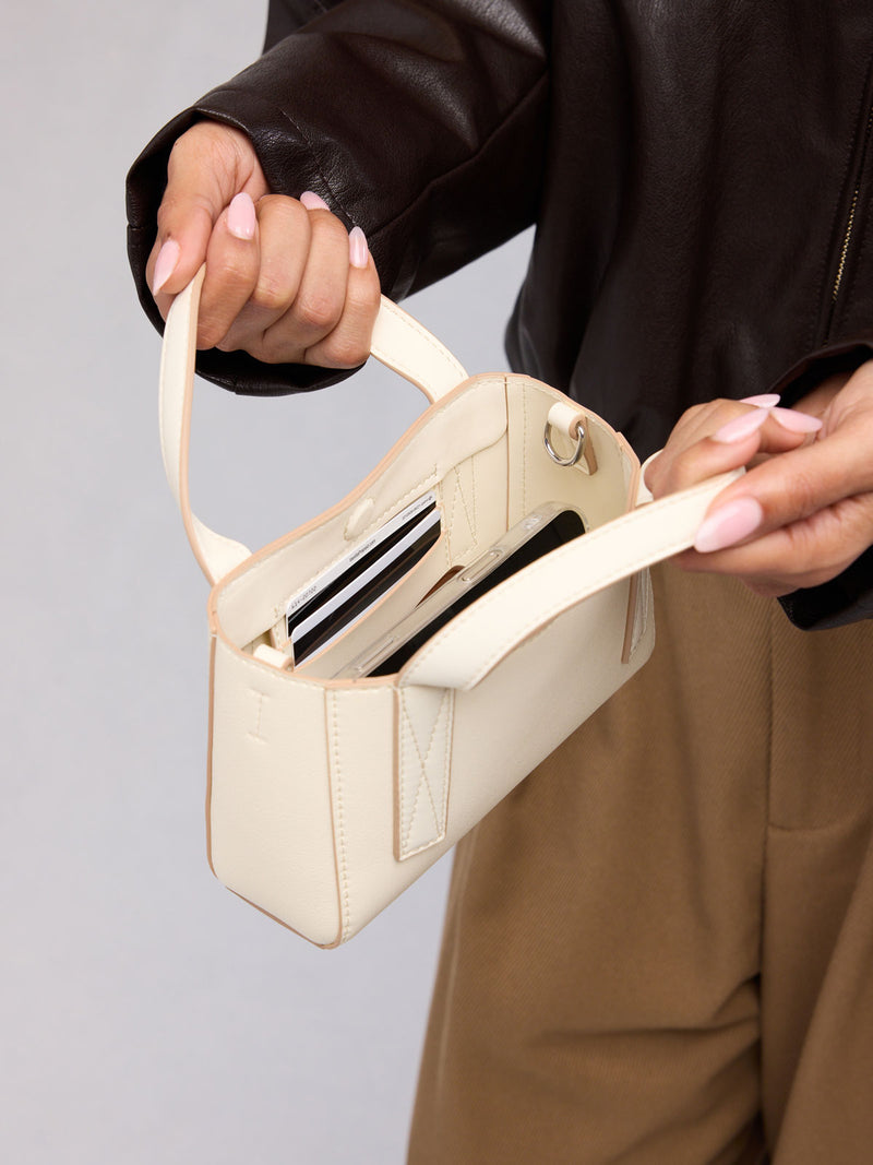Person holding open the CALPAK Haven Mini Crossbody Bag in beige Buttercream