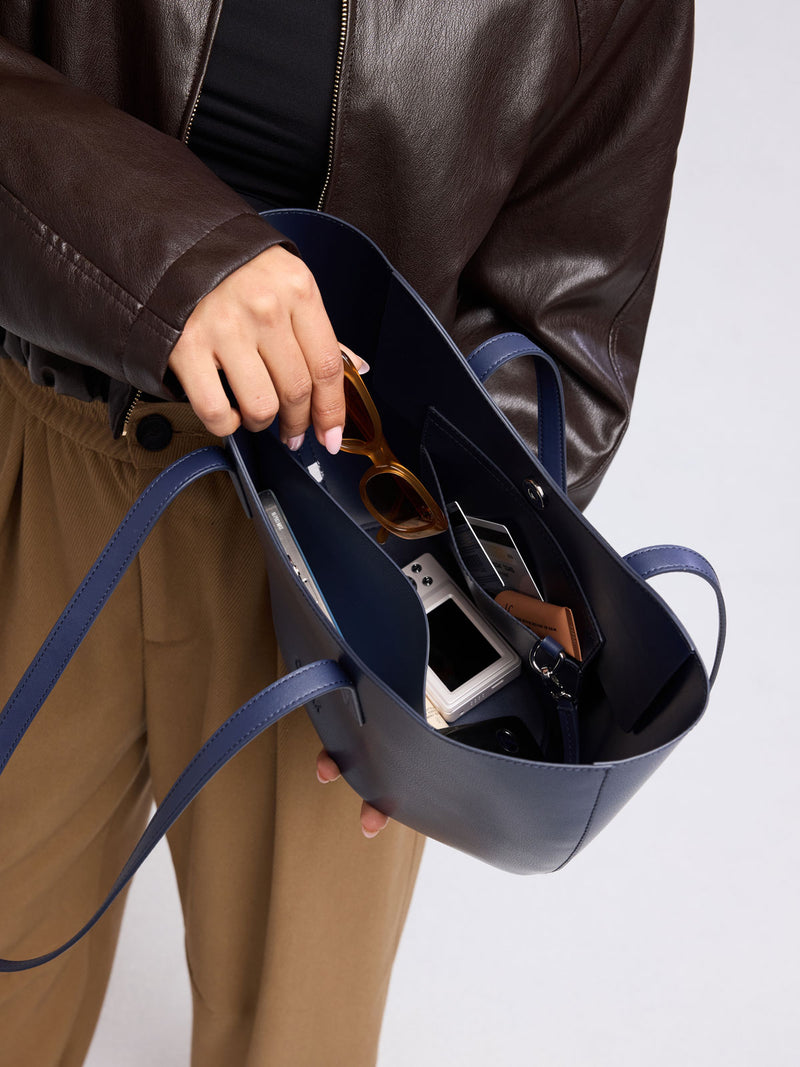 Person adding images into CALPAK Haven Tulip Tote in dark blue