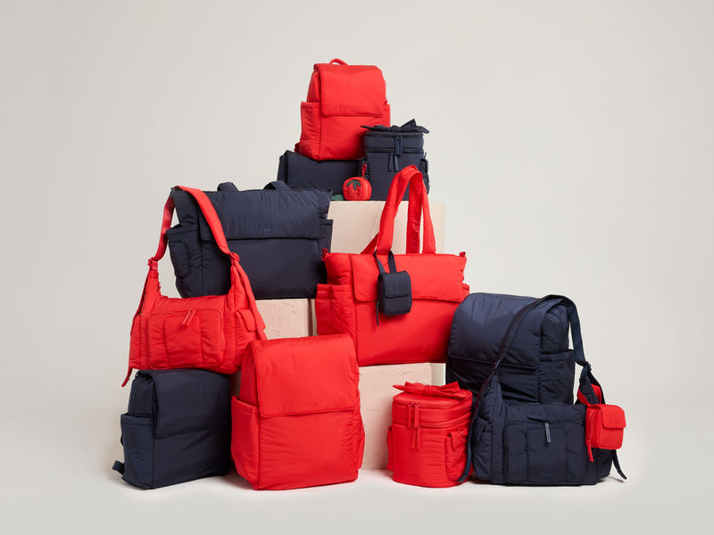 Collection of red and navy  CALPAK Baby Collection bags on a light gray background