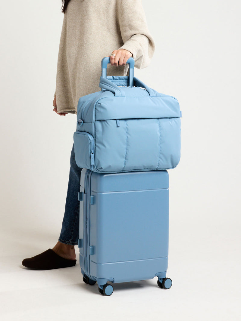 Model with CALPAK Hue Carry On Luggage in light blue French Blue