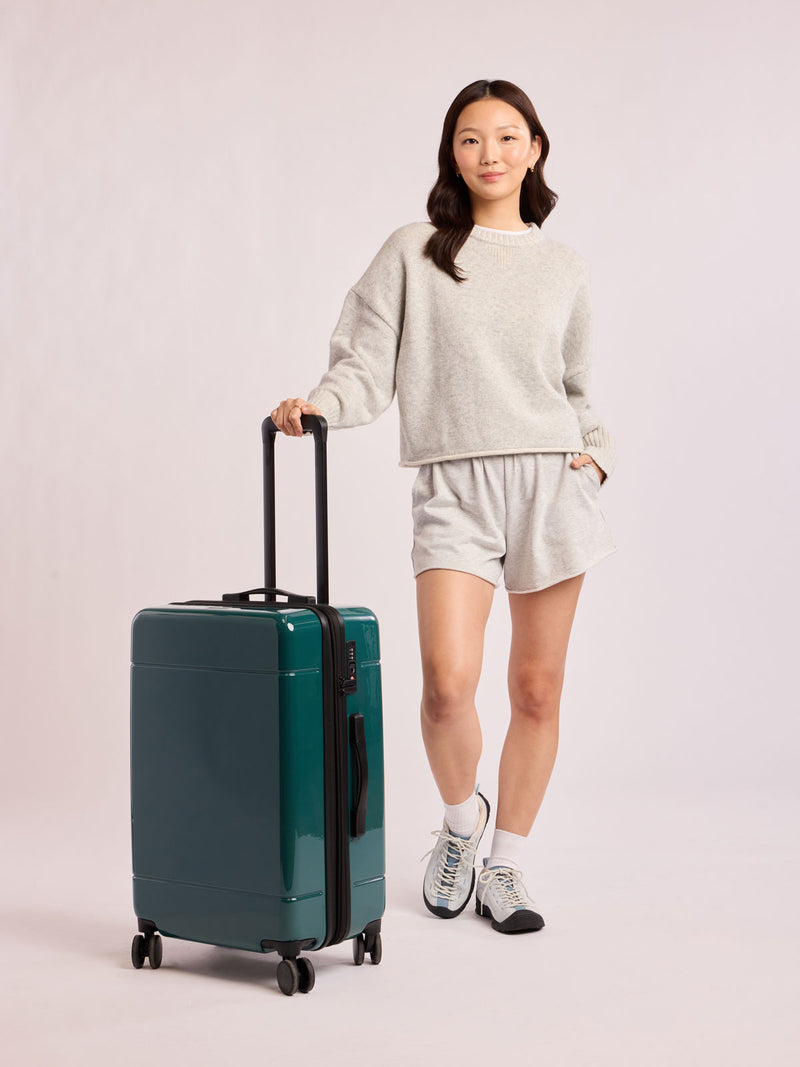 Woman wiht CALPAK Hue Medium Luggage in dark green Kale