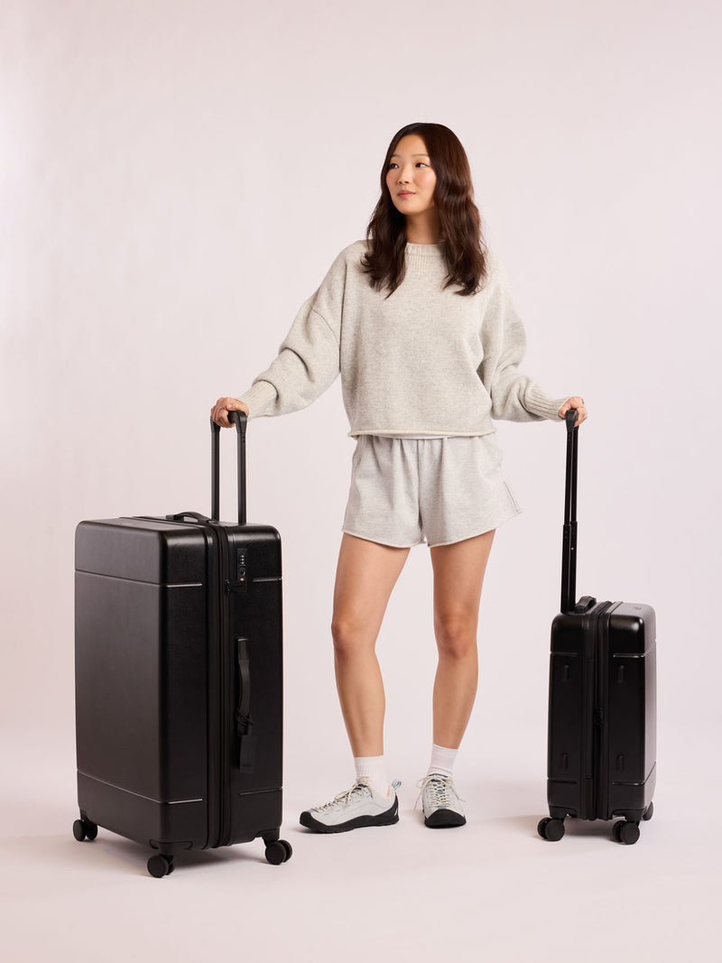 Person holding two black luggage as part of Hue Starter Bundle against a white background