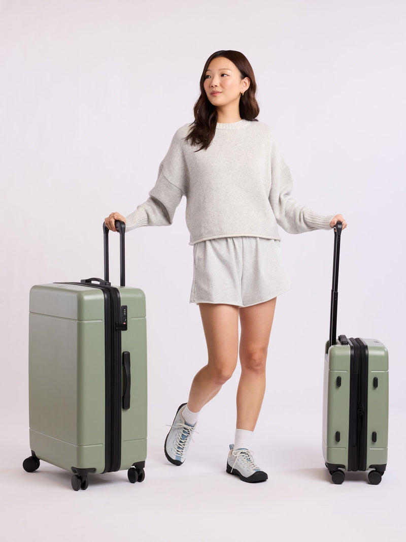 Woman holding two green CALPAK luggage part of Hue Starter Bundle on a white background