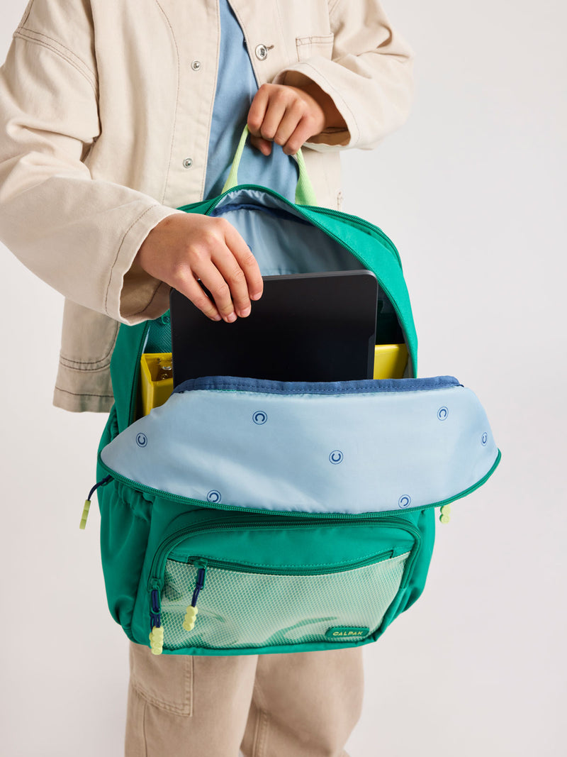 Child putting tablet into Green CALPAK Kids Large Backpack with lime green accents on a white background