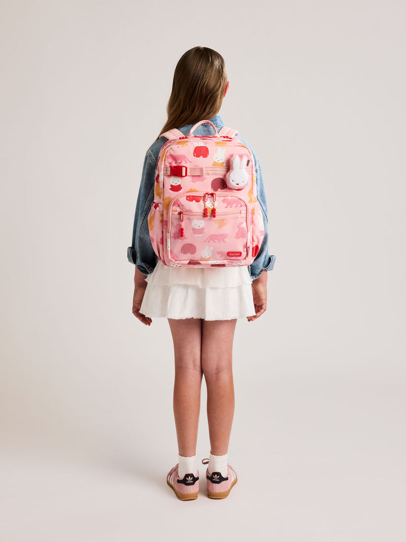 Girl wearing a CALPAK Kids Large Backpack with Miffy and pink colorful animal pattern on a white background