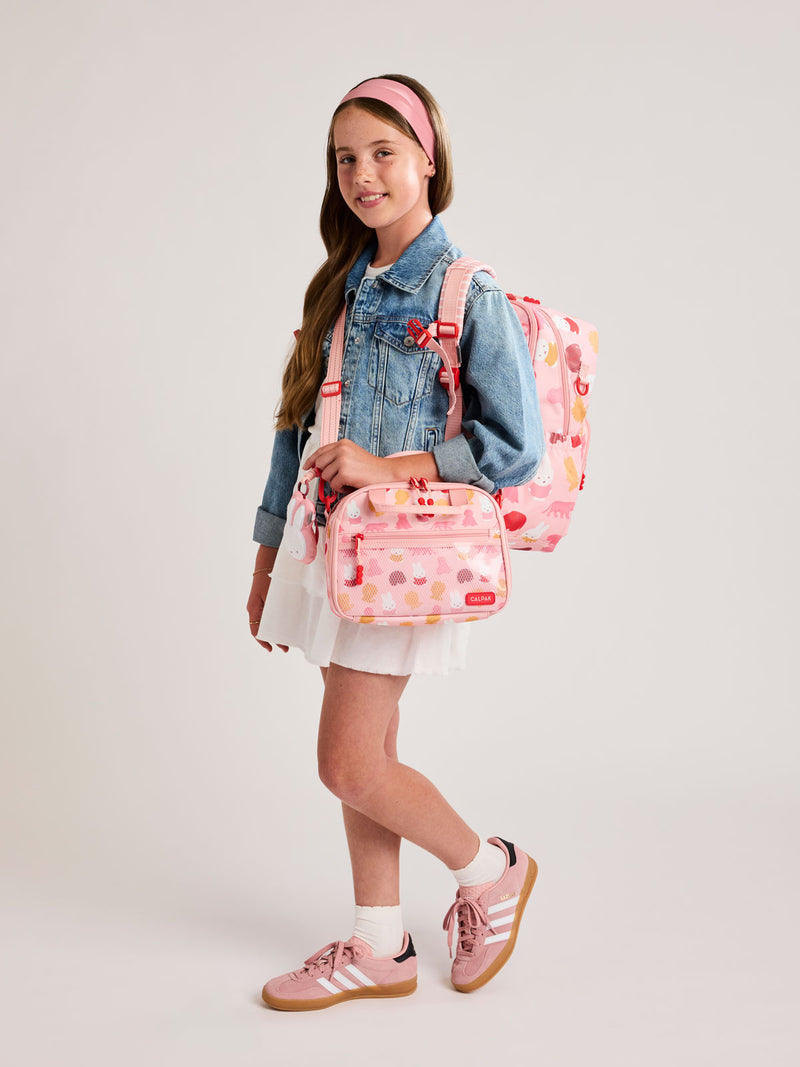 Girl wearing the Pink CALPAK Kids Lunch Bag with Miffy and animal pattern with mesh front pocket and top handles and the Miffy Kids Backpack on a white background