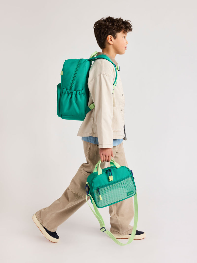 Child wearing a Green CALPAK Kids Medium Backpack  and matching CALPAK Lunch Bag with lime green accents on a white background