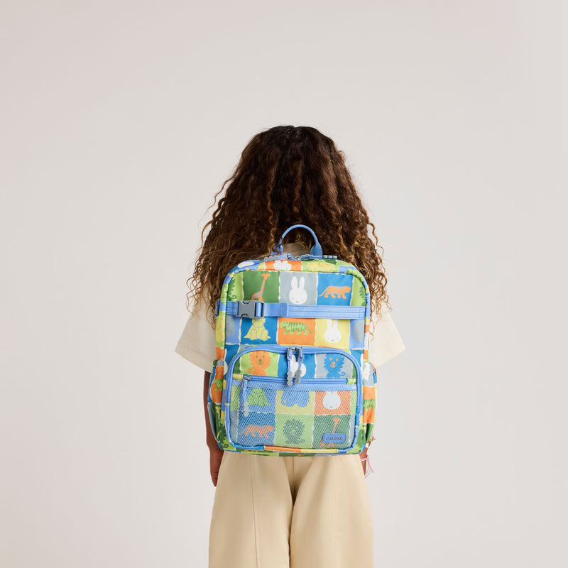 Child wearing the CALPAK + Miffy Medium Backpack in Miffy Blue Zoo Trip featuring Miffy and other animal characters with colorful tiles