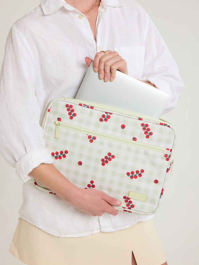 Person putting laptop into CALPAK 13"-14" Padded Laptop Sleeve in white and green gingham pattern with tomato print