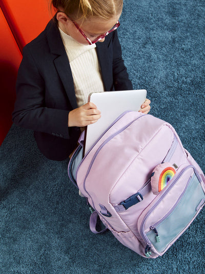 CALPAK Kids Collection Large Kids Backpack Bundle in pink lavender Orchid Pink that includes Kids Lunch Bag, Kids Pencil Case, Rainbow Pluffy Bag Charm, and Set of 2 Ice Packs in a kid's room; BCKL5000-ORCHID-PINK view 2