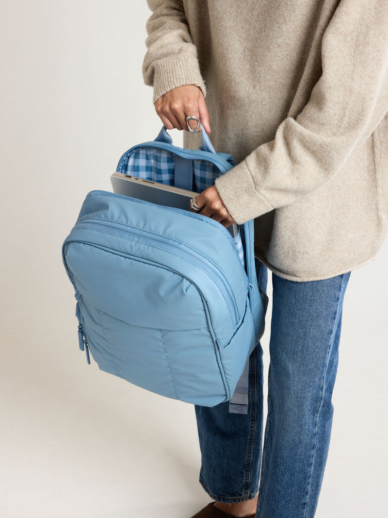 Person adding a laptop into the CALPAK Luka 15" Backpack in light blue French Blue