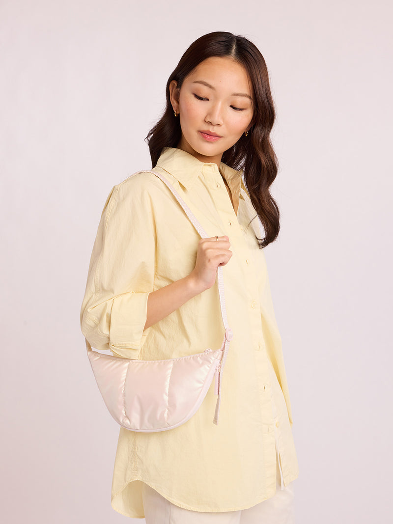 Woman with CALPAK Luka Crescent Bag in light pink shiny Pearlescent