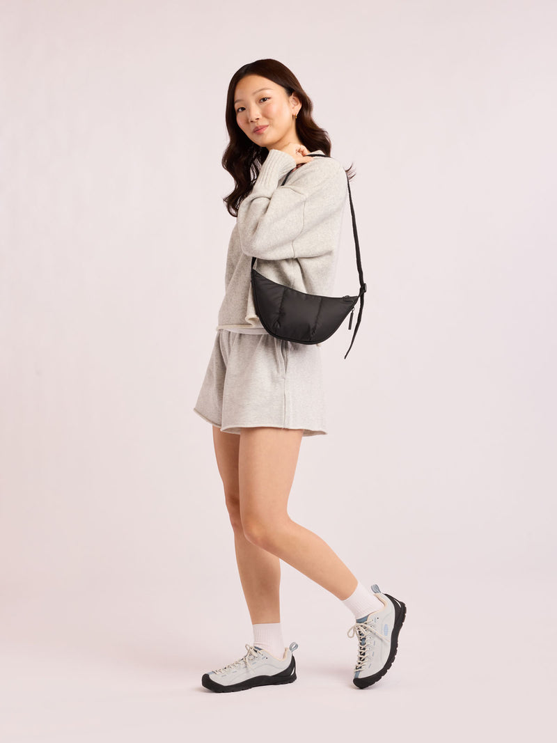 Model with grey outfit wearing CALPAK Luka Crescent Bag in Black