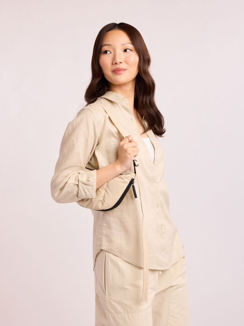 Model with beige outfit wearing CALPAK Luka Crescent Bag in beige off white Oatmeal