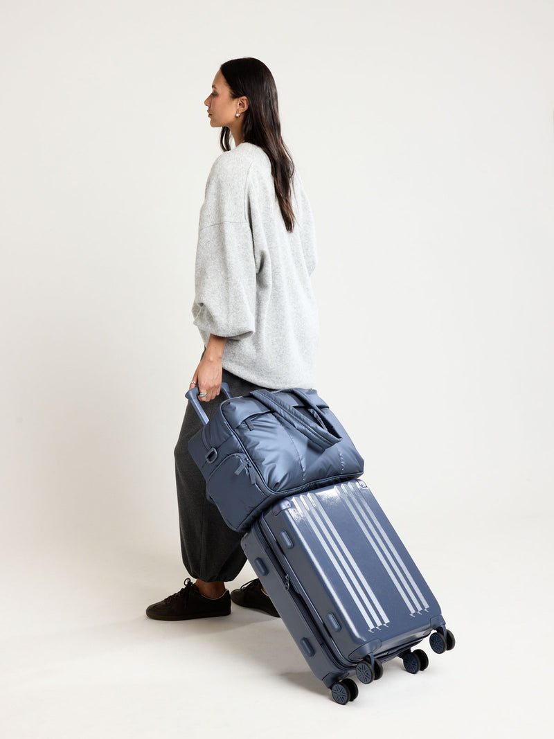 Woman carrying CALPAK Luka Duffel in metallic dark blue material Metallic Indigo